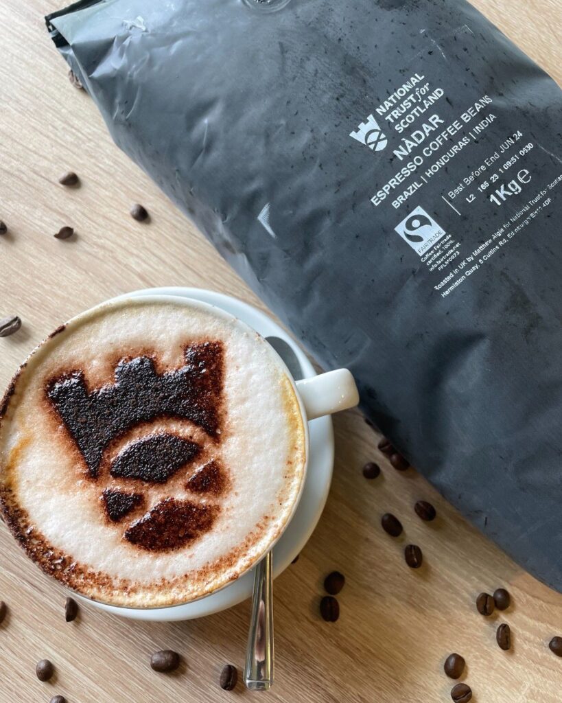 Bag of private label coffee for National Trust of Scotland next to a cappuccino with the NTS logo in chocolate topping